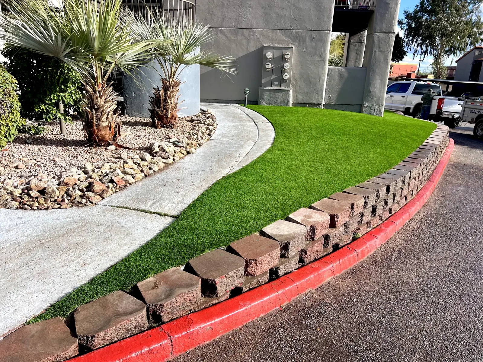 Curved turf installation with stone border and clean pathway at a multifamily property.